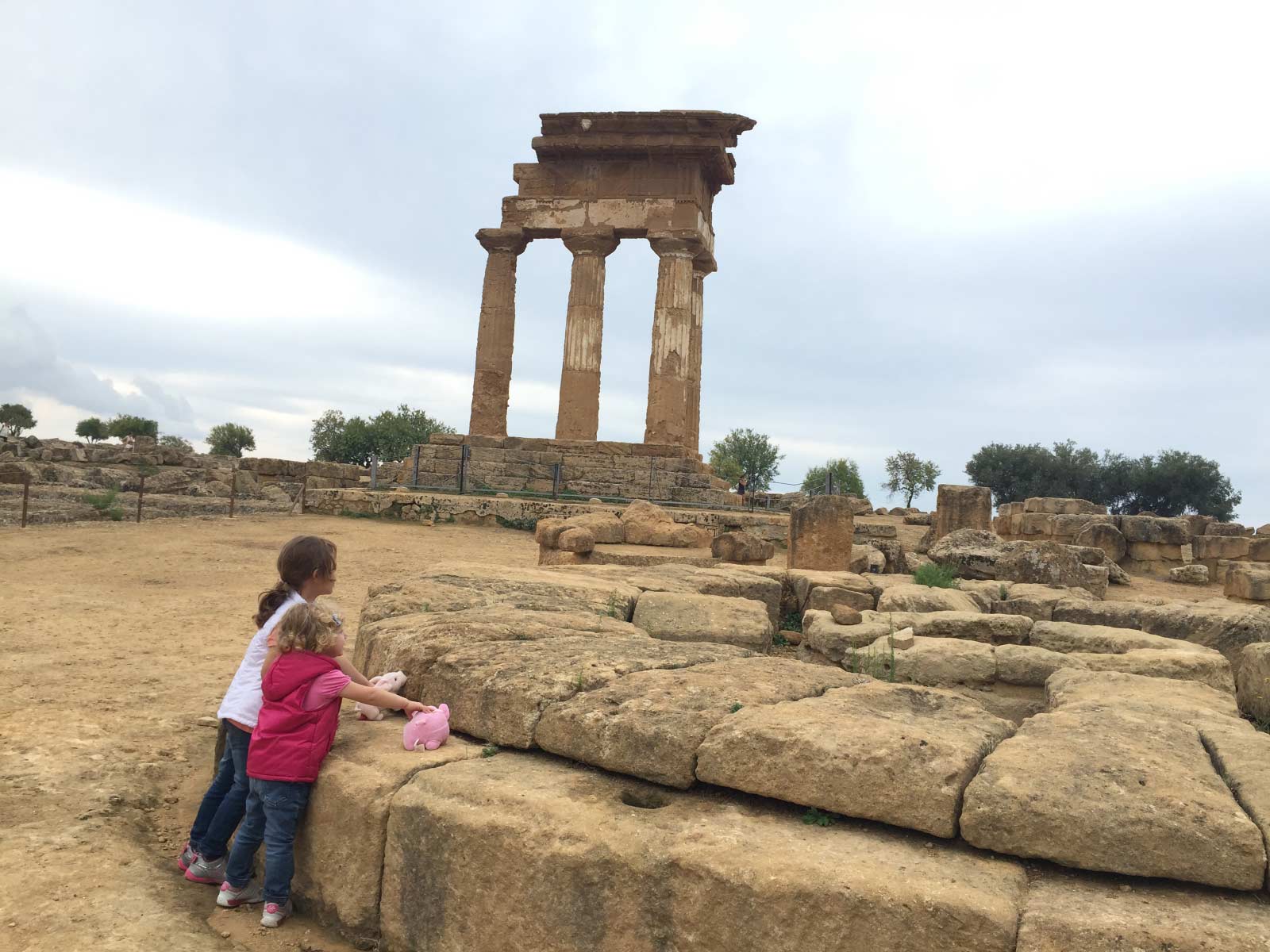 Due bambine offrono i maialini di peluche sull'altare circolare di Demetra con il tempio dei Dioscuri sullo sfondo
